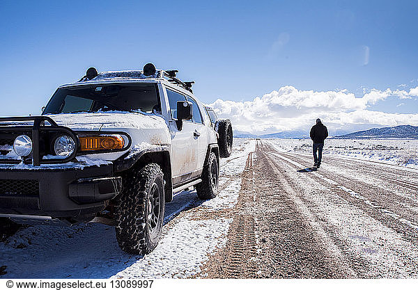 Rückansicht eines Mannes mit Geländewagen auf unbefestigter Straße inmitten der Wüste im Winter