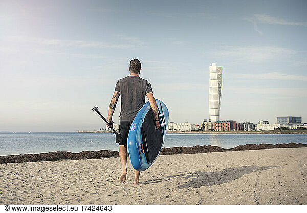 Rückansicht eines Mannes mit Stand Up Paddleboard am Strand