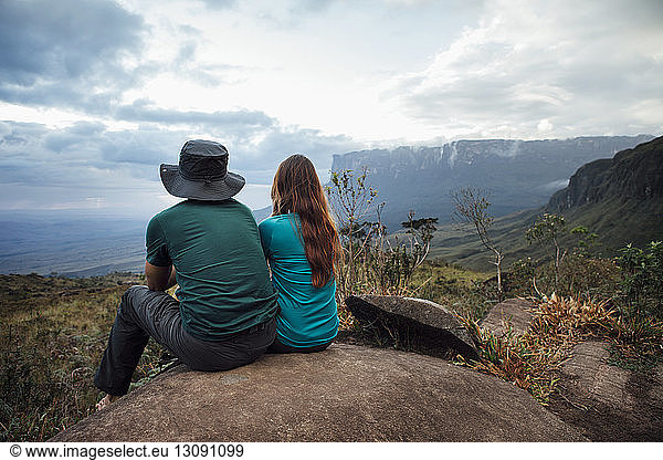 Rückansicht eines Mannes und einer Frau die auf einem Felsen gegen den Himmel sitzen