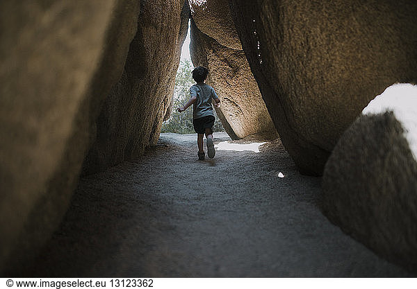Rückansicht eines unter Felsformationen laufenden Jungen im Joshua-Tree-Nationalpark