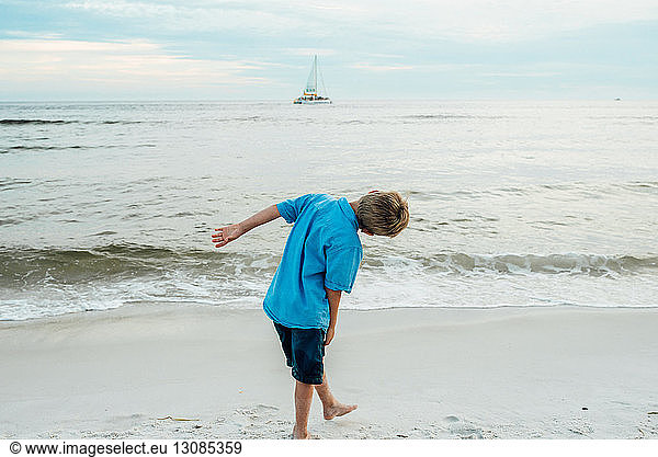 Rückansicht eines verspielten Jungen  der sich am Strand von Panama City gegen den Himmel beugt
