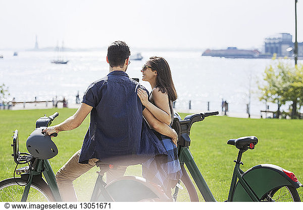 Rückansicht eines zärtlichen Paares mit Fahrrädern im Park am Fluss