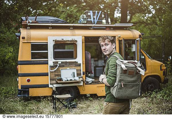 Rückansicht Porträt eines Mannes mit Rucksack auf dem Weg zum Wohnmobil im Wald beim Camping