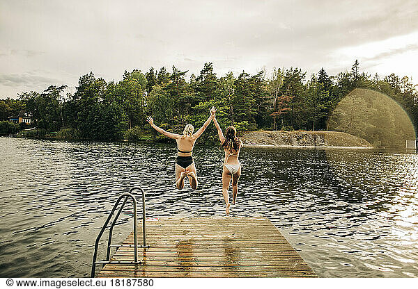 Rückansicht von Freundinnen im Bikini beim Springen im See im Urlaub