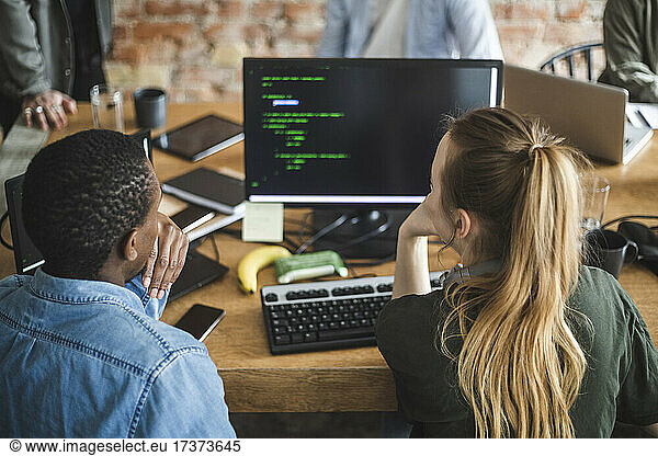 Rückansicht von männlichen und weiblichen Kollegen  die in einem Start-up-Unternehmen am Computer arbeiten