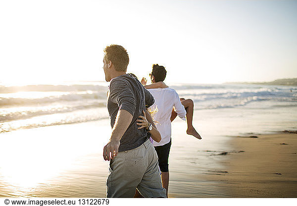 Rückansicht von Paaren  die am Strand gegen den klaren Himmel laufen