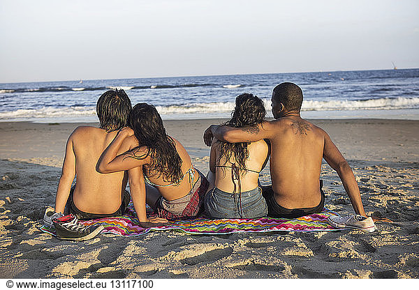 Rückansicht von Paaren  die an einem sonnigen Tag am Strand sitzen
