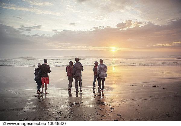 Rückansicht von Paaren  die bei Sonnenuntergang am Strand am Ufer spazieren gehen