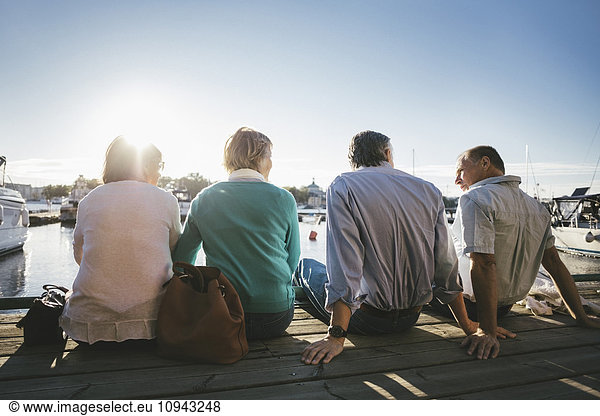 Rückansicht von zwei älteren Paaren  die auf dem Pier gegen den klaren Himmel sitzen.