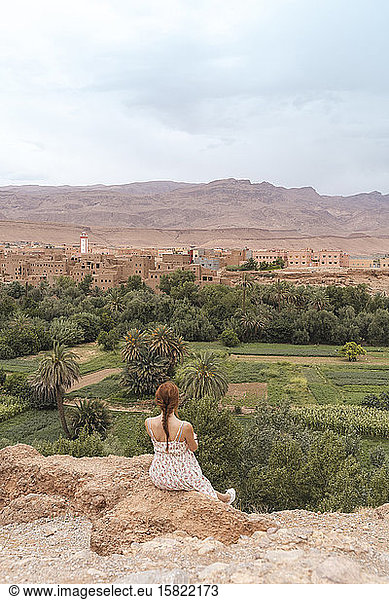 Rückenansicht einer jungen Frau  die auf einem Felsen sitzt und auf die Stadt schaut  Ouarzazate  Marokko