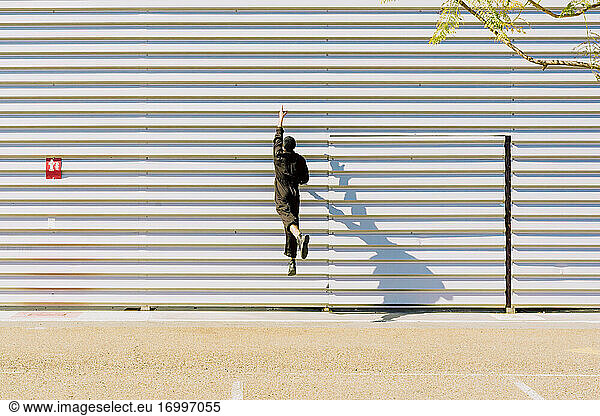 Rückenansicht eines Mädchens in schwarzem Overall  das vor einem Industriegebäude in die Luft springt