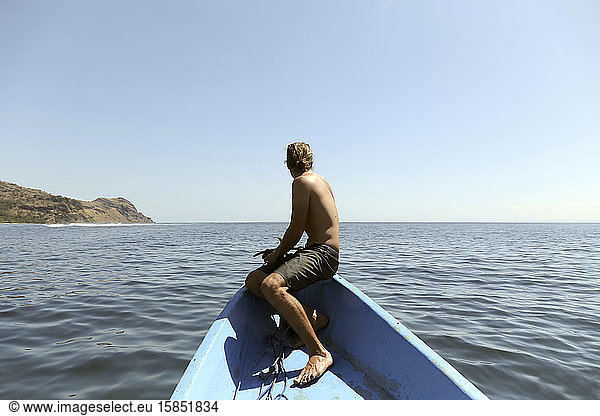 Rückenansicht eines Mannes  der am Bug eines Bootes sitzt