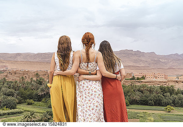 Rückenansicht von drei jungen Frauen  die Arm in Arm stehen und auf die Stadt blicken  Ouarzazate  Marokko
