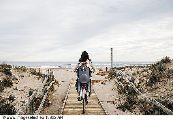 Radfahrende Frau auf einer Strandpromenade in den Dünen mit Tochter im Kindersitz
