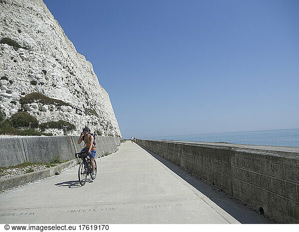 Radfahrer ohne Hemd entlang der weißen Kreidefelsenpromenade mit Meer  Brighton  East Sussex  UK; Brighton  East Sussex  England