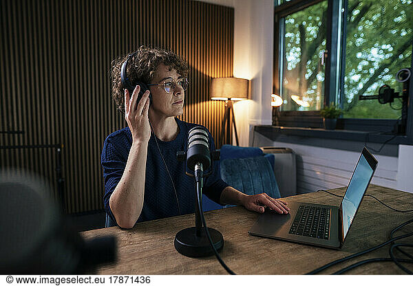 Radio DJ sitting with microphone and laptop at desk in recording studio