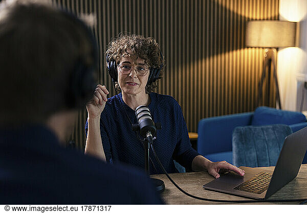Radio DJ wearing eyeglasses and headset interviewing guest in recording studio