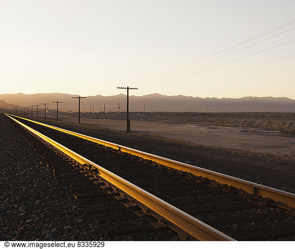 Railroad tracks extending across the flat Utah desert landscape  at dusk.