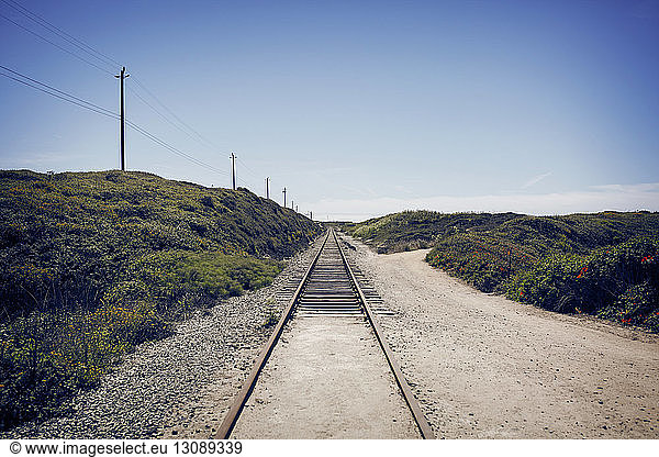 Railroad tracks on field against blue sky