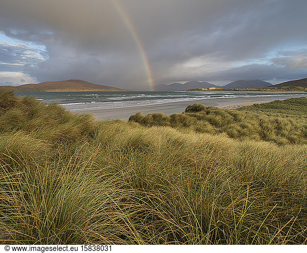 Rainbow shines above sea and coastal sand dunes at Seilebost beach  Isle of Harris  Scotland