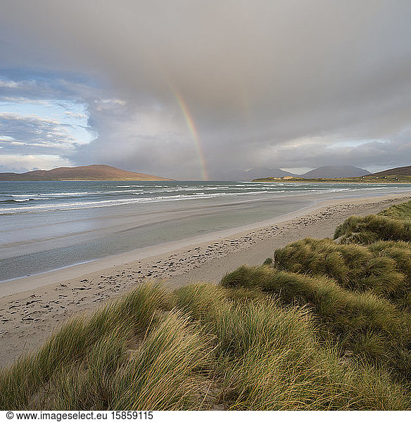 Rainbow shines above sea and coastal sand dunes at Seilebost beach  Isle of Harris  Scotland