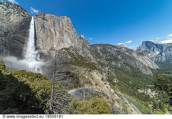 Rainbow stretching across valley created from waterfall flowing above