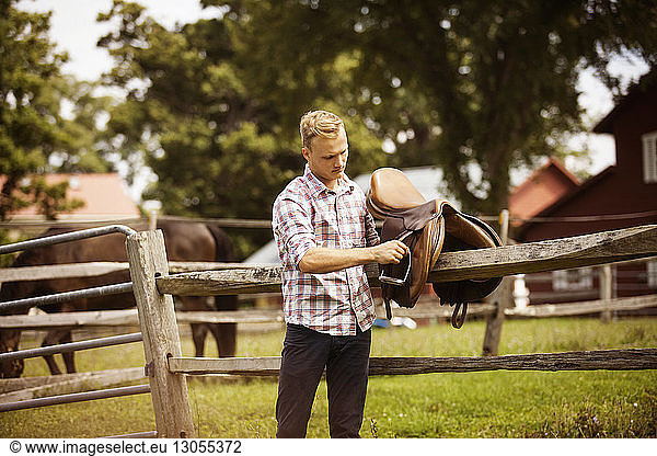 Rancher with saddle by fence in farm