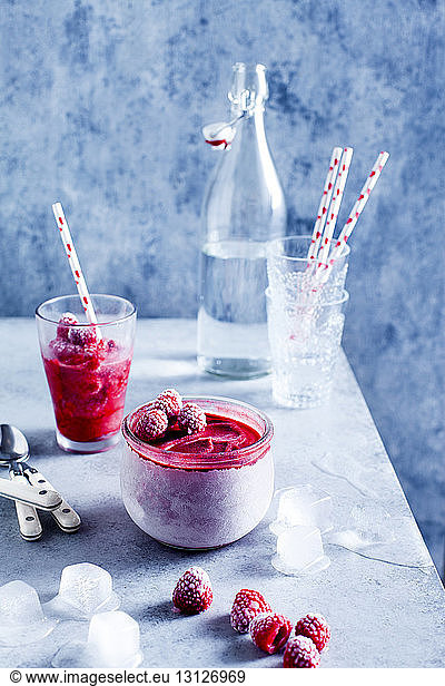 Raspberries sorbet with drinking glasses and straws by bottle on marble table