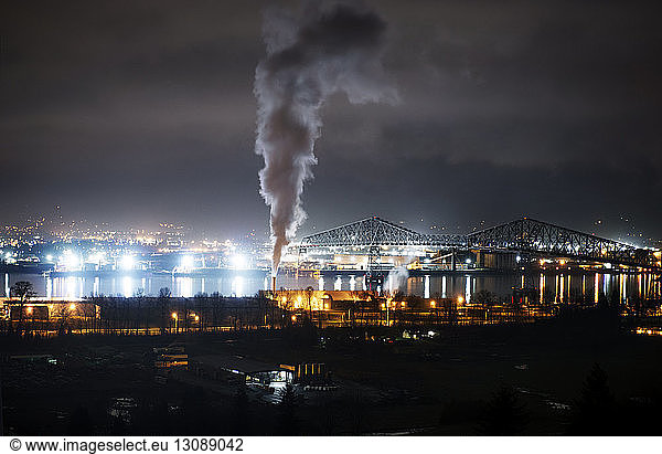 Rauch aus dem Schornstein einer Fabrik in einer beleuchteten Stadt bei Nacht