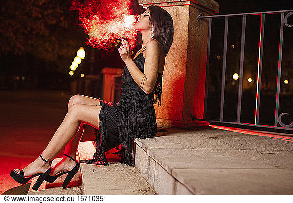 Rauchende junge Frau in schwarzem Abendkleid  die nachts auf einer Treppe sitzt