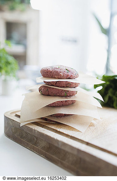 Raw hamburger patties stacked between parchment paper