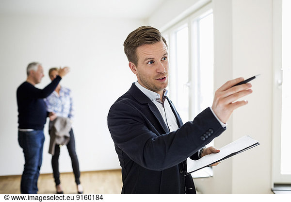 Real estate agent examining house with couple discussing in background