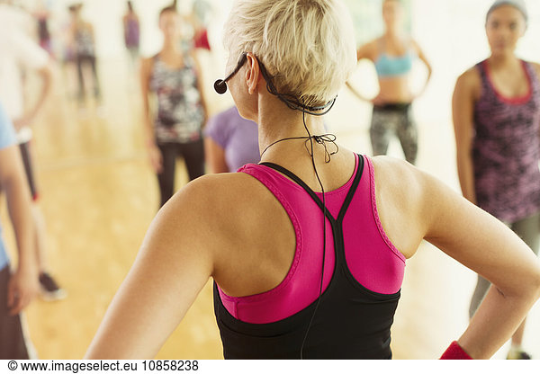 Rear view fitness instructor with headset leading aerobics class