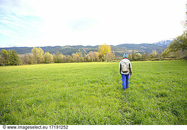 Rear view of a backpacker woman walking on green meadow.