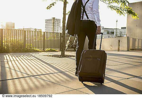 Rear view of a businessman pulling wheeled luggage at sunset  Munich  Bavaria  Germany