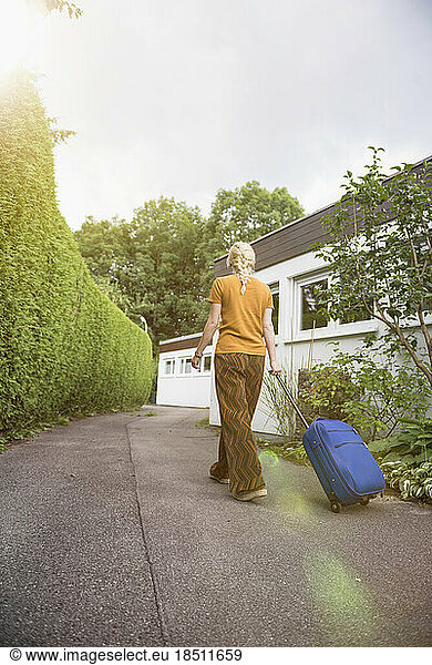 Rear view of a young woman with luggage leaving the house  Munich  Bavaria  Germany