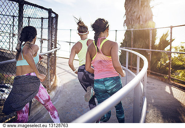 Rear view of athletes jogging on bridge against sky