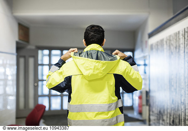 Rear view of auto mechanic student wearing reflective jacket in workshop