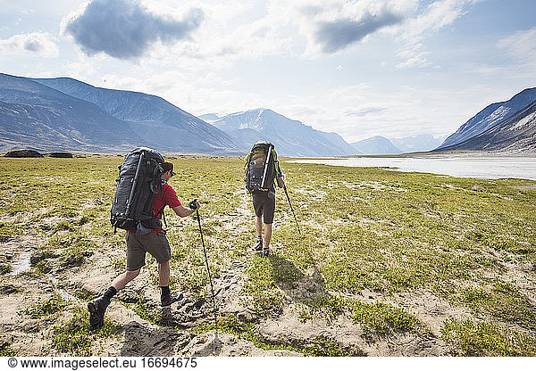 Rear view of Backpackers hike over arctic tundra in Akshayak Pass