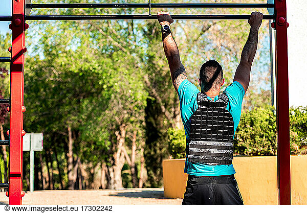 Rear view of Bearded brunette man doing a barbell pull-up with weight vest. Outdoor fitness concept.