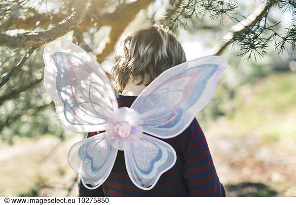 Rear view of boy in fairy wings at yard