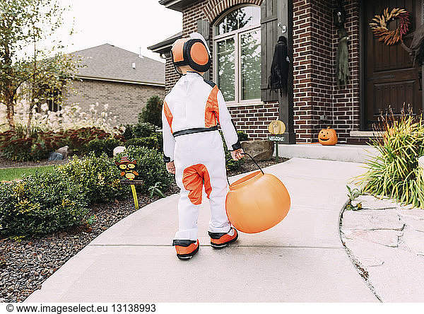 Rear view of boy in Halloween costume with container walking in yard