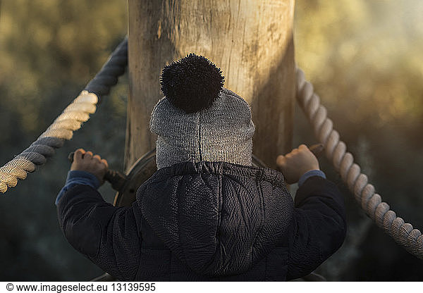Rear view of boy in warm clothing spinning steering wheel at playground