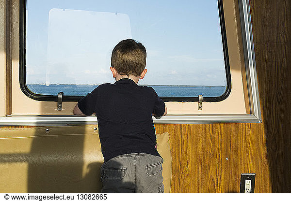 Rear view of boy looking through window while travelling in boat