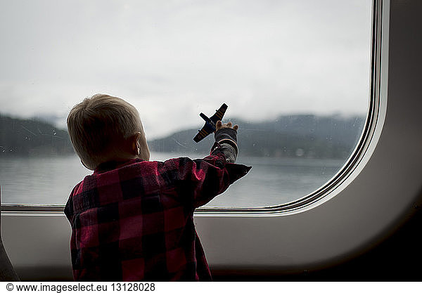 Rear view of boy playing with toy plane while travelling in train