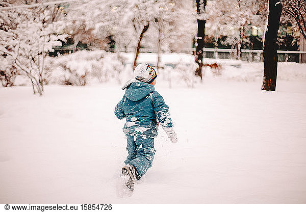 Rear view of boy running in snow covered field in park in winter