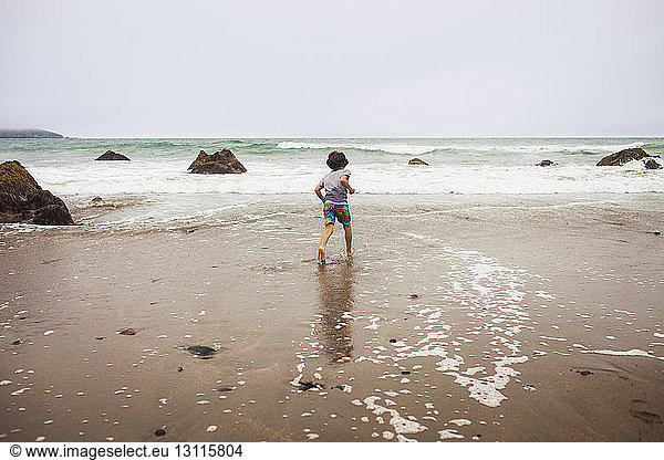 Rear view of boy running on wet shore