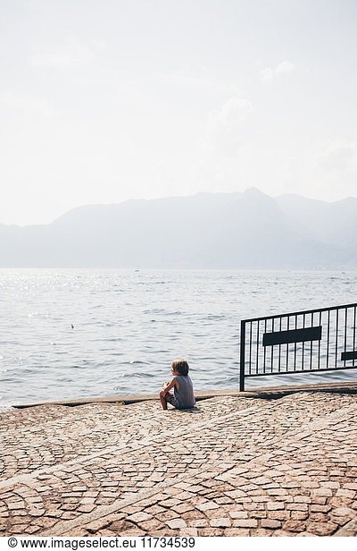 Rear view of boy sitting cobbled steps looking out at view  Luino  Lombardy  Italy