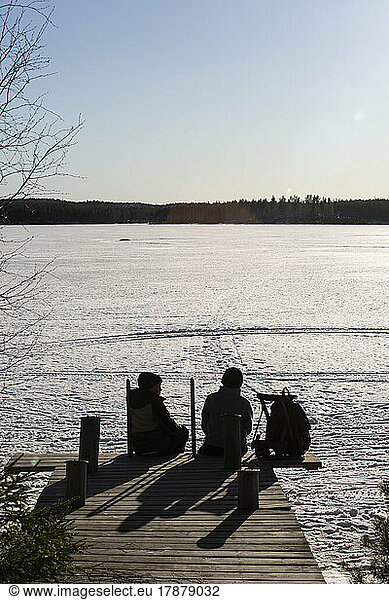 Rear view of boys sitting on jetty over frozen lake during sunny day