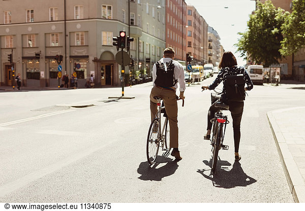 Rear view of business colleagues riding bicycle on city street